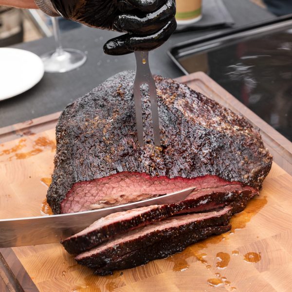 Chef carving a portion of succulent marinated spicy beef brisket on a wooden chopping board in close up high angle on the knife blade