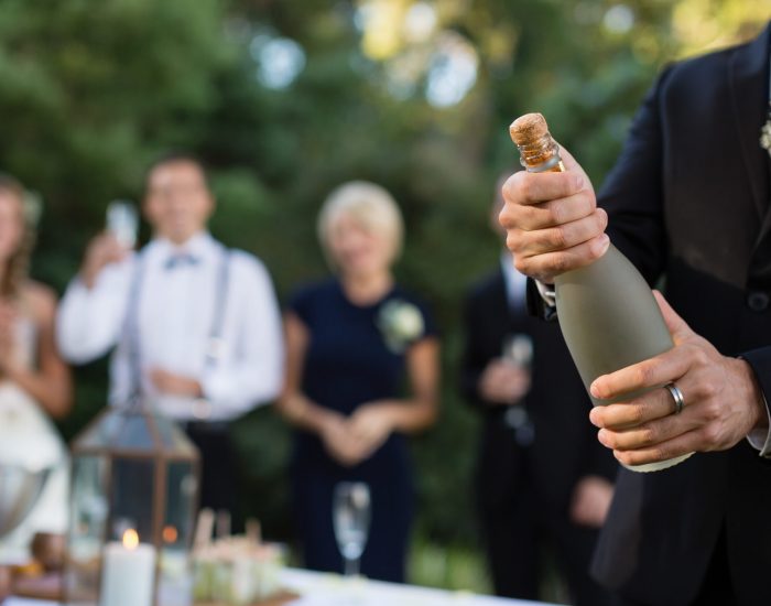Mid section of groom opening champagne bottle at park